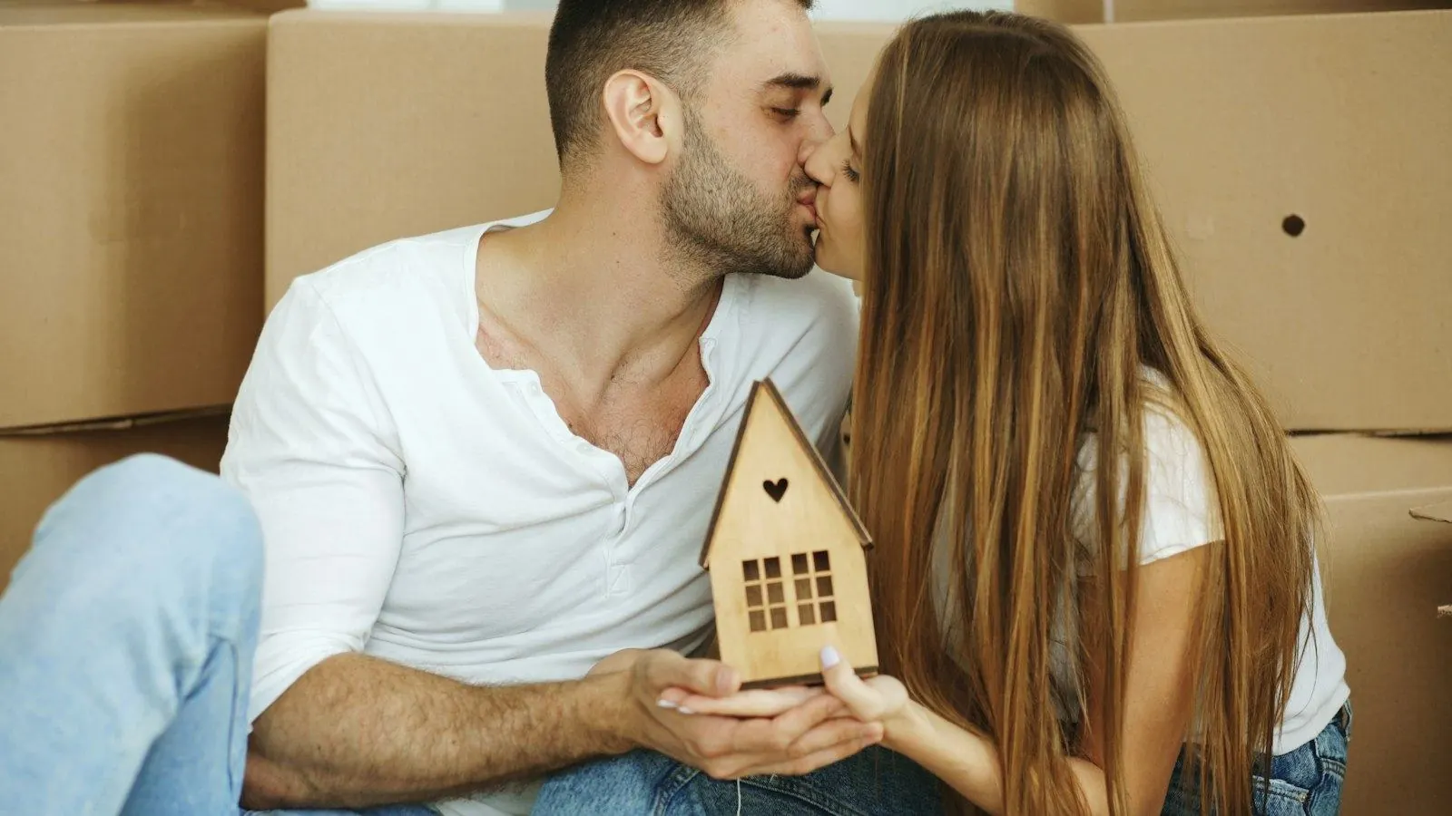 Couple holding a small wooden house among moving boxes